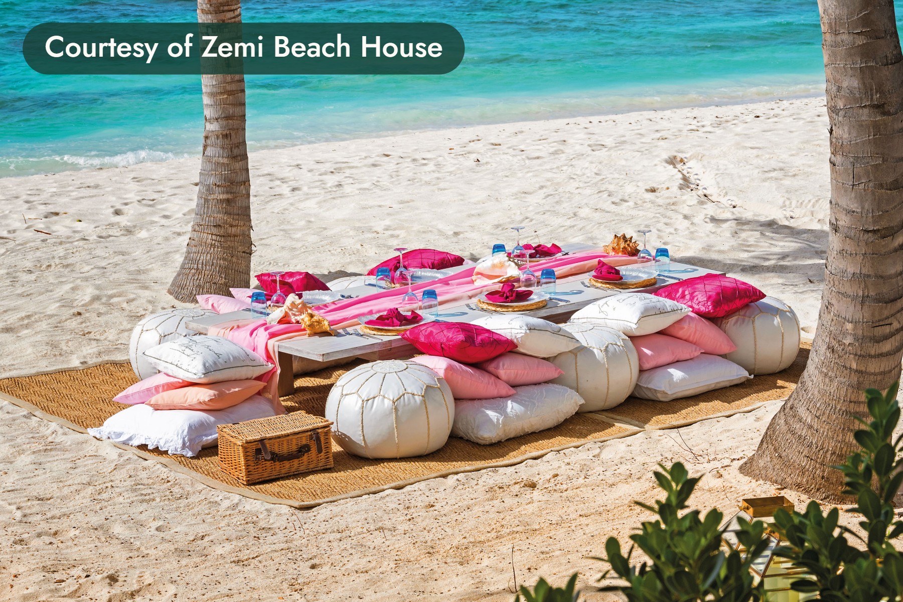 A beach picnic of pink cushions and white poufs between two palms in Anguilla. Courtesy of Zemi Beach House.