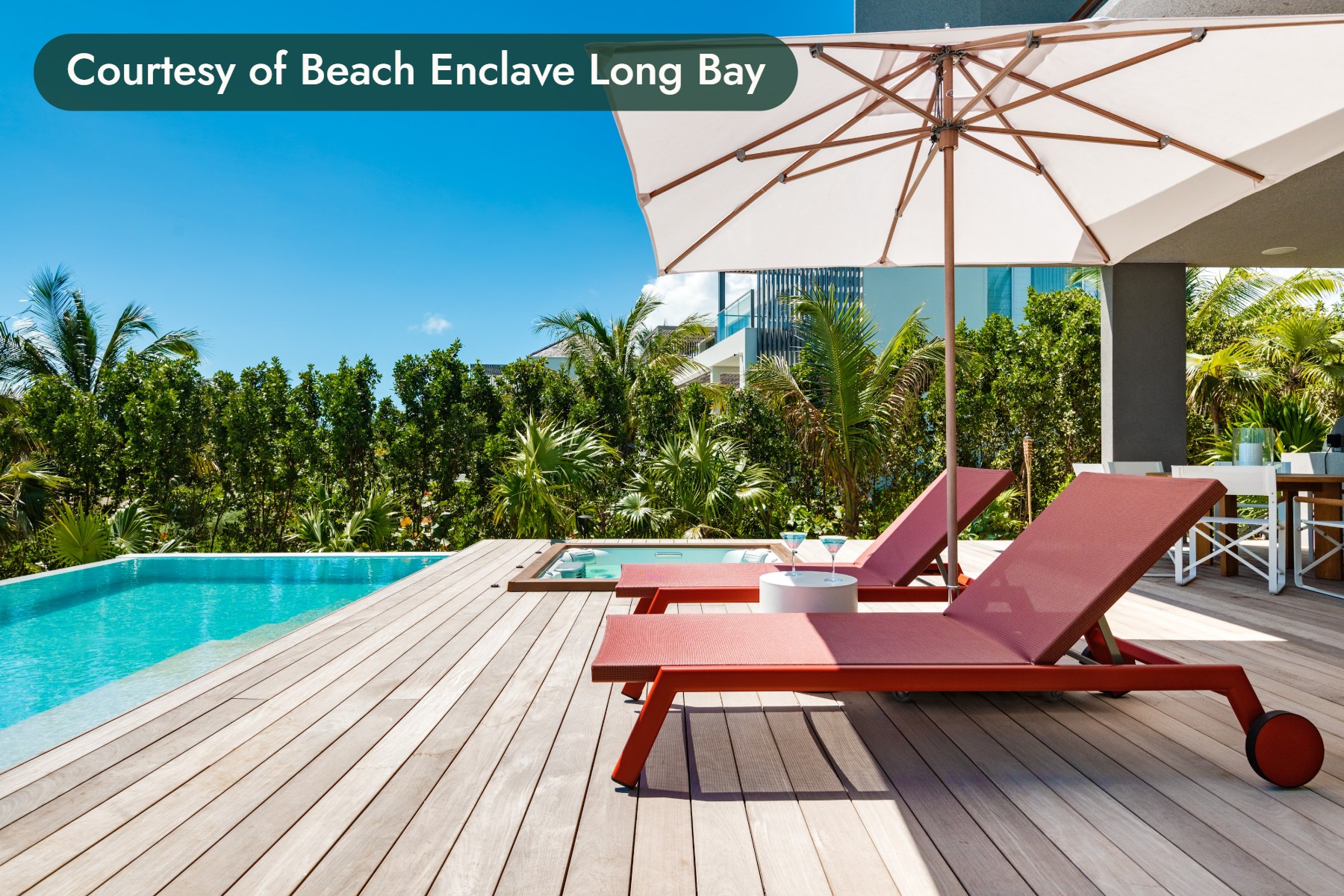 Red loungers and a white umbrella on a pool deck framed by palms in Turks and Caicos. Courtesy of Beach Enclave Long Bay.