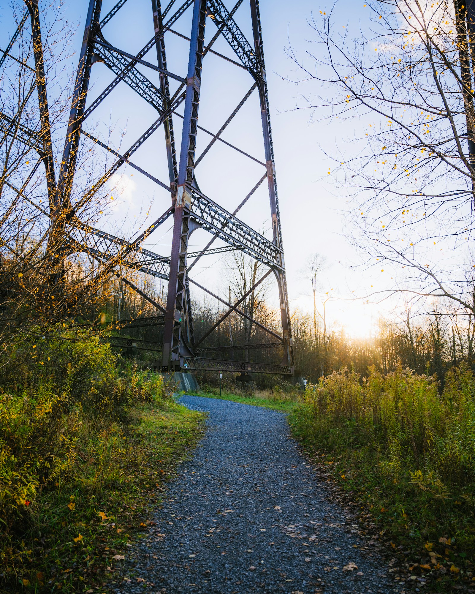 A gravel path leads under the steel tower of the Kinzua Bridge at sunset, with autumn trees on both sides.