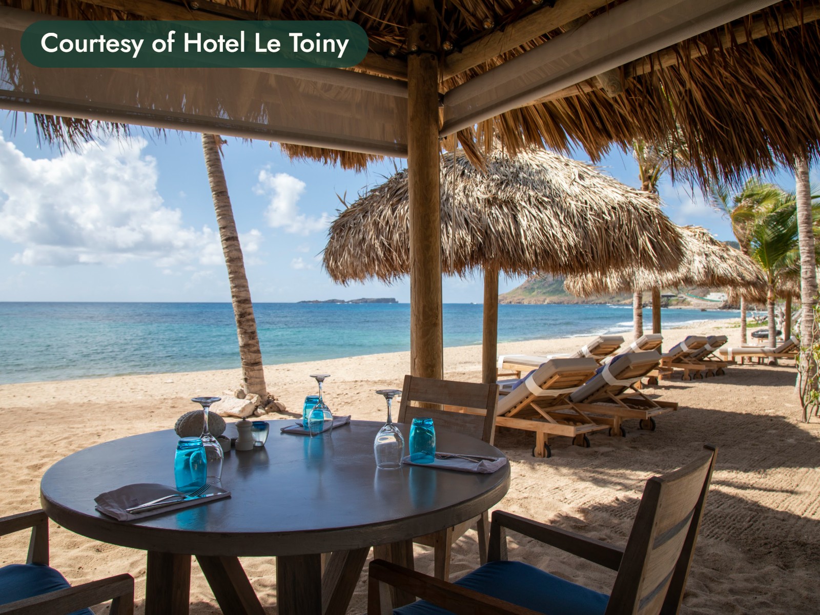 A table set for lunch under a thatched roof on the beach in St. Barths. Courtesy of Hotel Le Toiny.