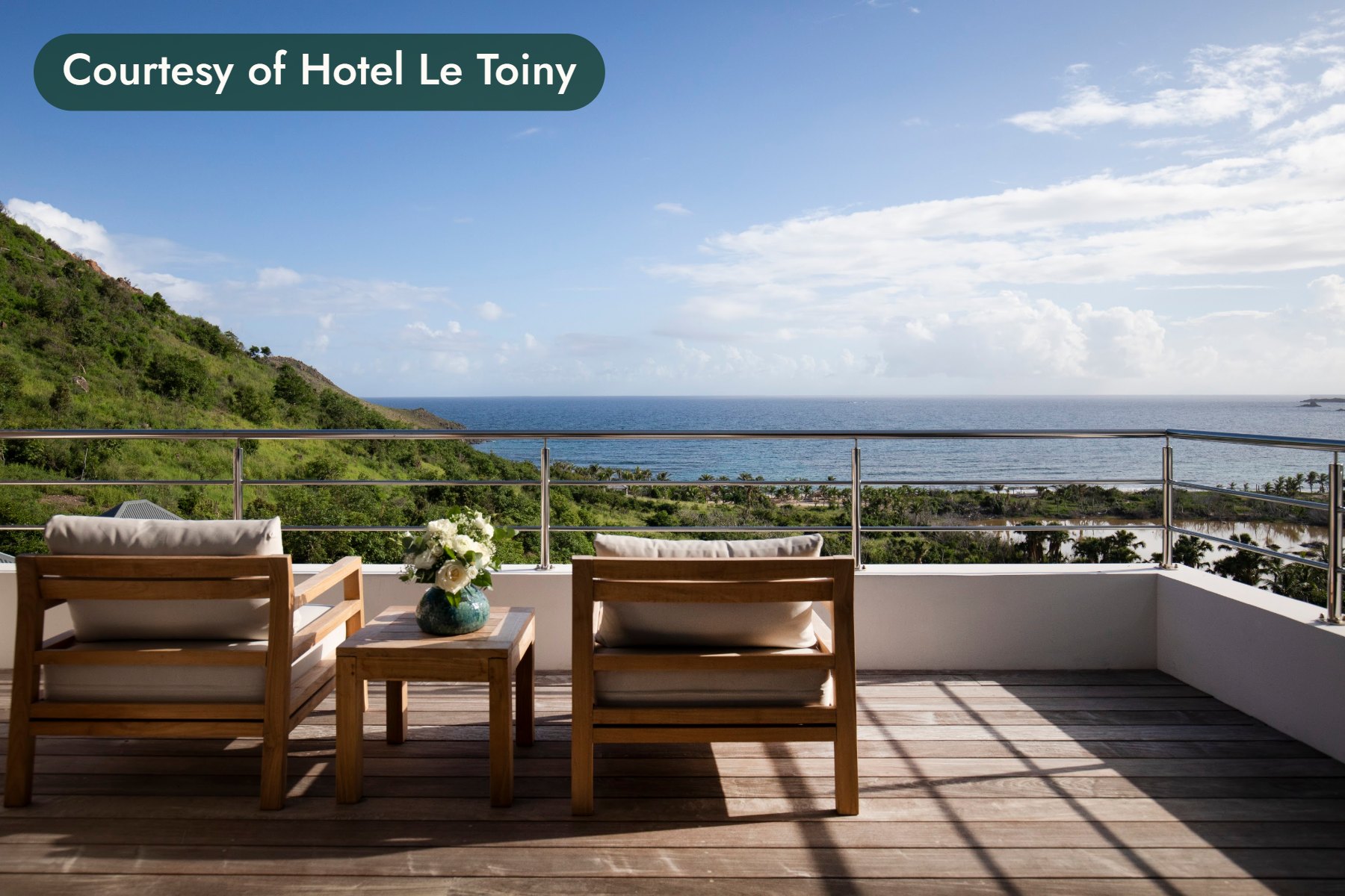 Two teak armchairs and a vase of white flowers on a suite terrace overlooking the sea in St. Barths. Courtesy of Hotel Le Toiny.