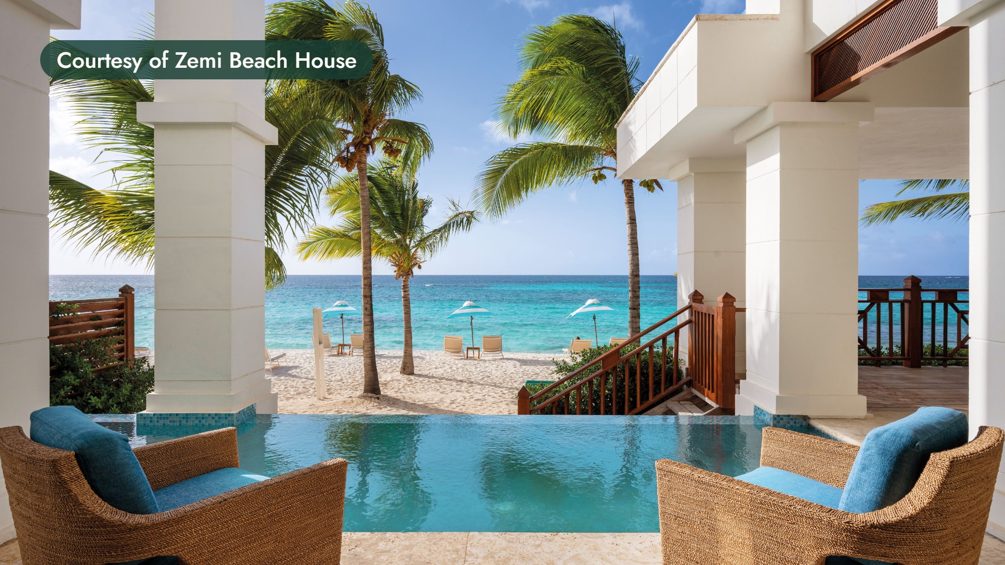 A plunge pool and two wicker armchairs on a terrace framed by white columns and palms, looking out to a white-sand beach in Anguilla. Courtesy of Zemi Beach House.