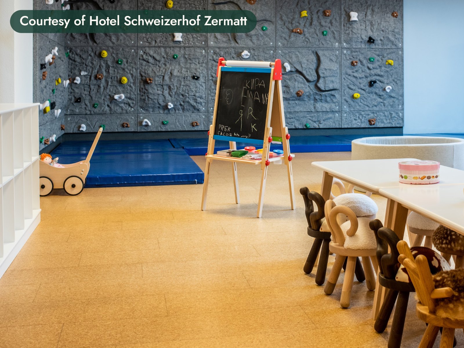 A bright playroom with a climbing wall, an easel and small wooden chairs at a low table. Courtesy of Hotel Schweizerhof Zermatt.