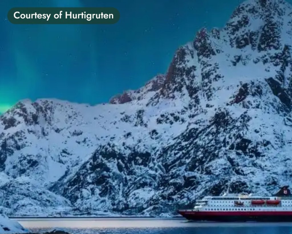 Cruise ship below snowy peaks under the northern lights. Courtesy of Hurtigruten.