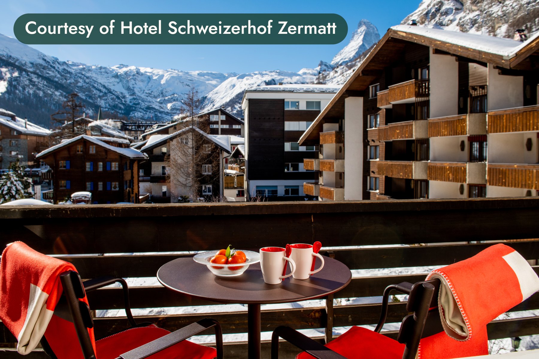 A balcony table with two mugs and a bowl of fruit, facing snowy peaks above Zermatt. Courtesy of Hotel Schweizerhof Zermatt.